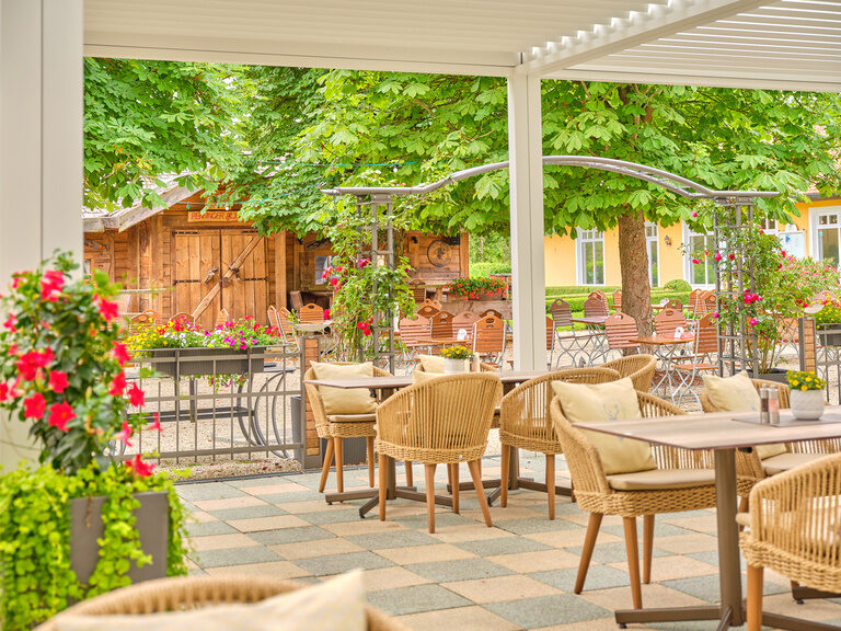 Sonnige Terrasse eines Restaurants mit einladendem Ambiente und Blumenarrangements.