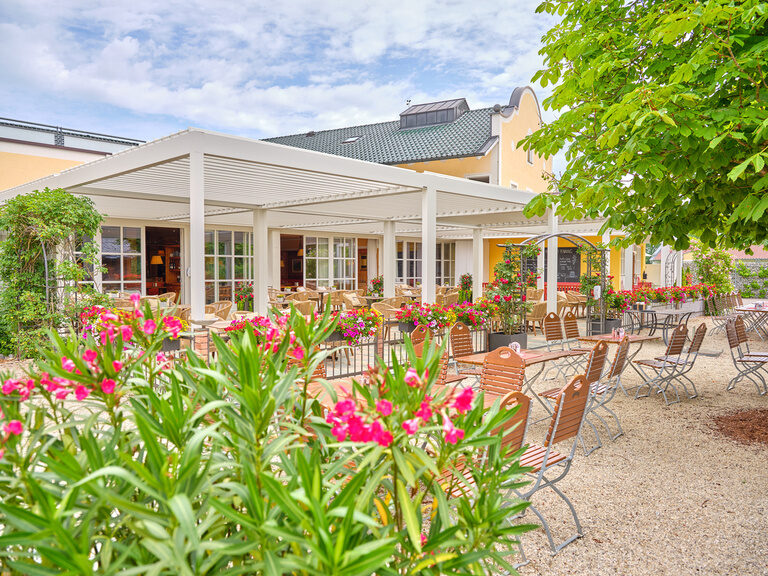 Gemütlicher Außenbereich eines Cafés mit blühenden Pflanzen und rustikalem Charme.